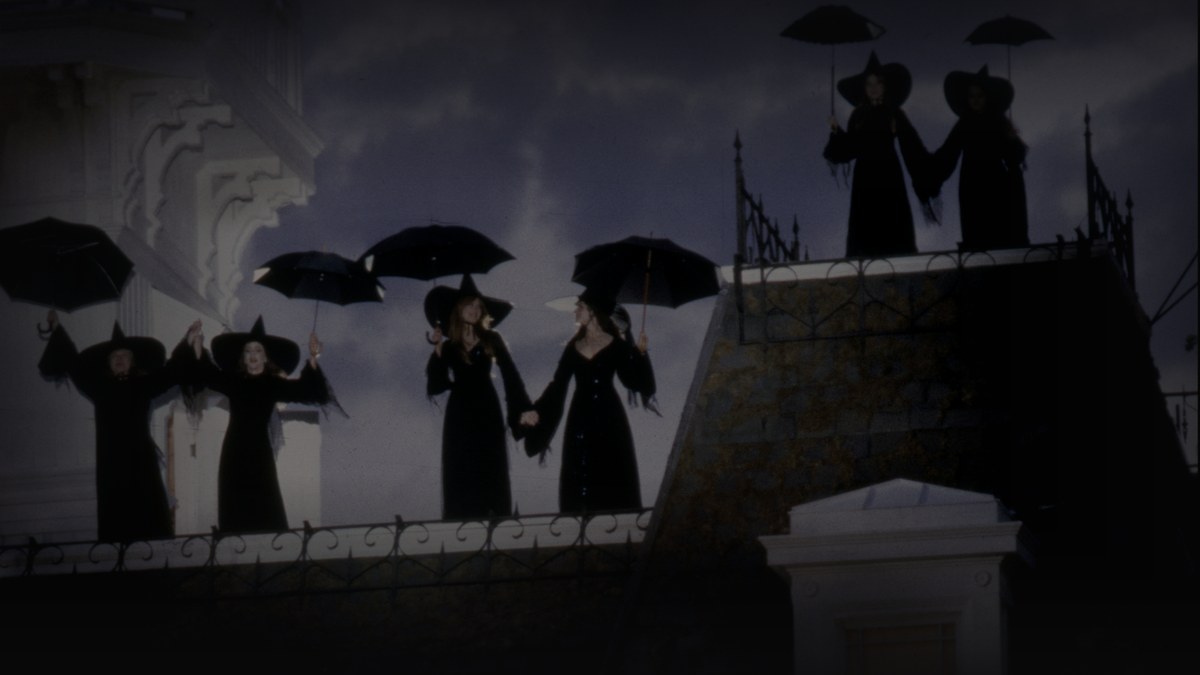 Still from Practical Magic (1998) — tmdb backdrop; genuine film still of the owens women on the mansion rooftop. baked through scripts/bake_dark_photo.py at factor 0.45, 1200x675